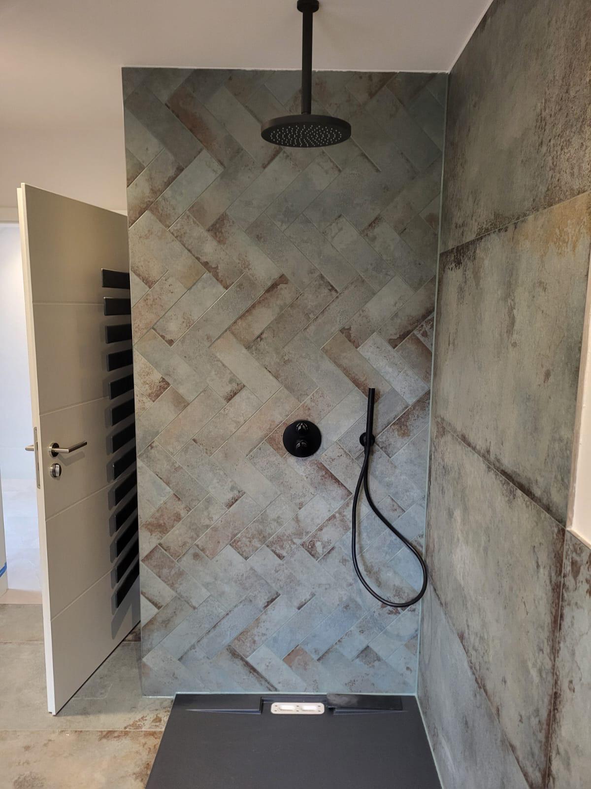 Dusche Fischgräte Moderne Dusche mit grauen Fliesen und schwarzem Duschkopf an einer strukturierten Wand.