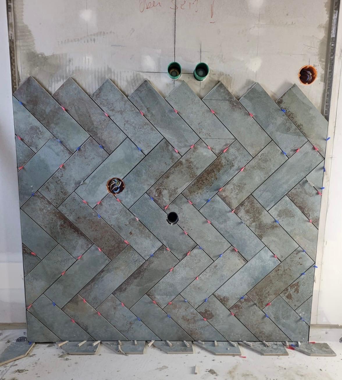 Fischgräte Muster aus grauen Fliesen in Fischgrätenanordnung an einer Wand.