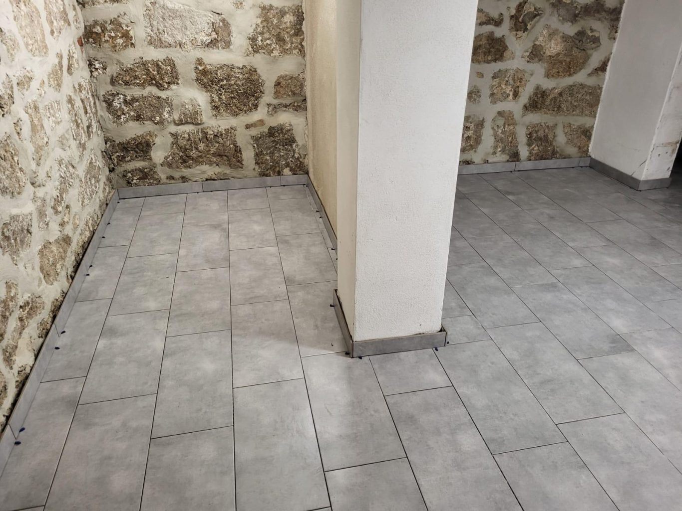 Kellerfussboden Raum mit grauem Fliesenboden und einer Steinwand im Hintergrund.