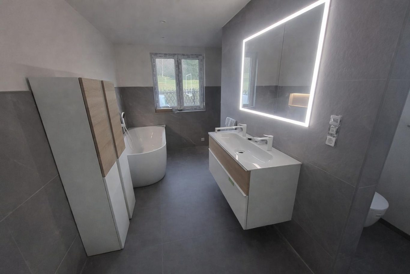 Fertiges Badezimmer Helles modernes Badezimmer mit Badewanne, Doppelwaschbecken und beleuchtetem Spiegel.