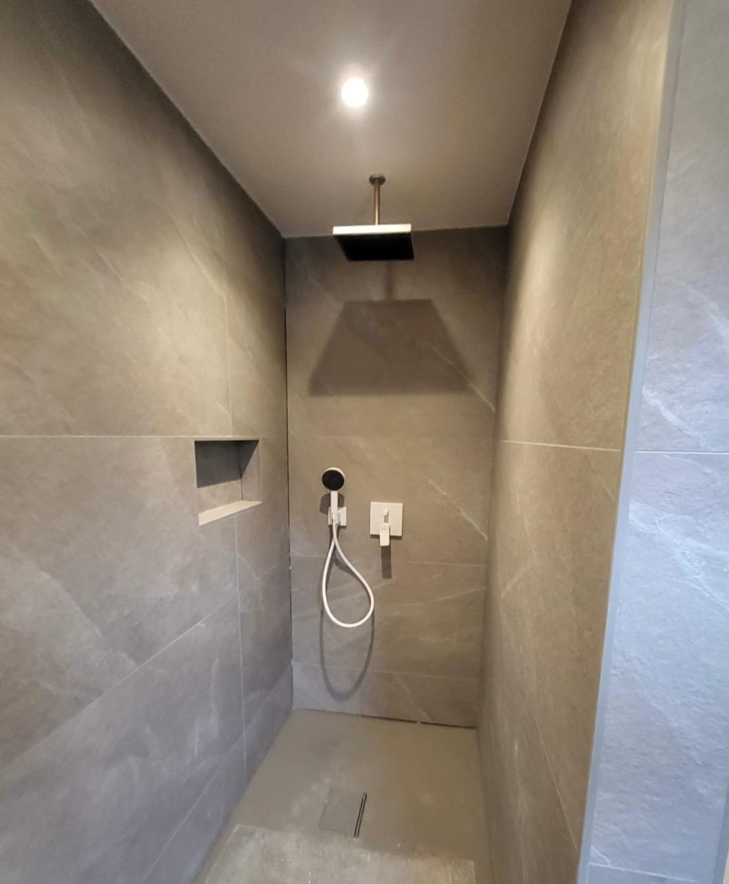 Dusche mit Shampoogarage Moderne Duschkabine mit grauen Wänden und Regenschauer-Duschkopf.