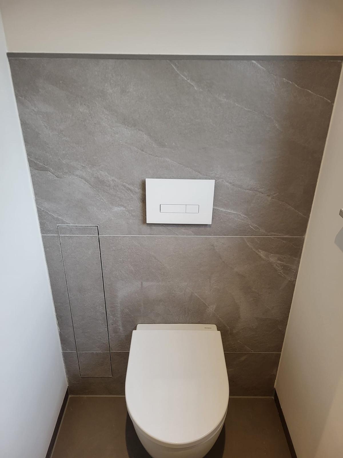 Fertig befliestes Toilettenelement Weiße Toilette vor einer grauen Wand mit Betätigungsplatte.