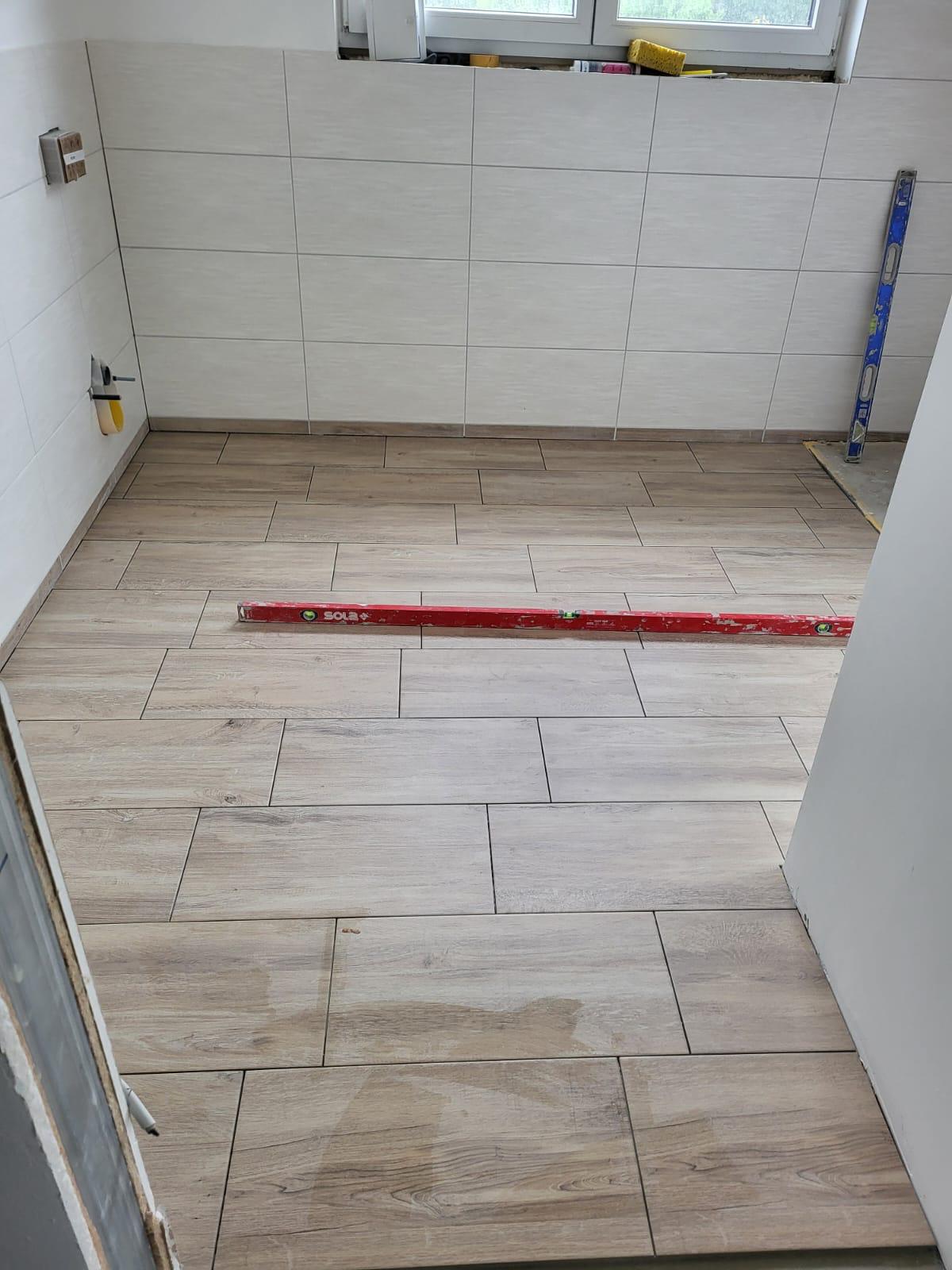 Badfussboden Fliesenboden in einem Raum, teilweise verlegt, mit einer Wasserwaage und Maßstab.